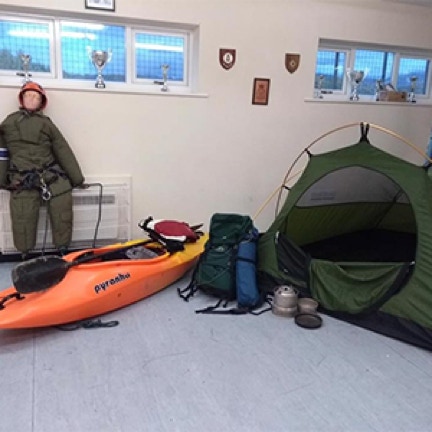 Shows a kayak, tent, rucksack and camping equipment